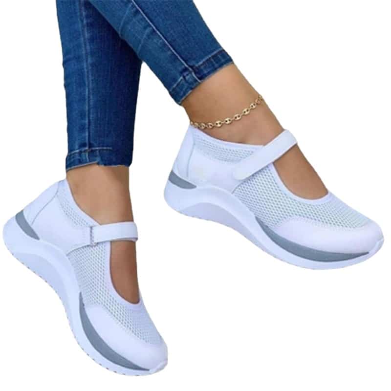Les baskets blanches sur des pieds de femme jambes croisées portant un jean slim bleu et un bracelet de cheville sur un fond blanc.