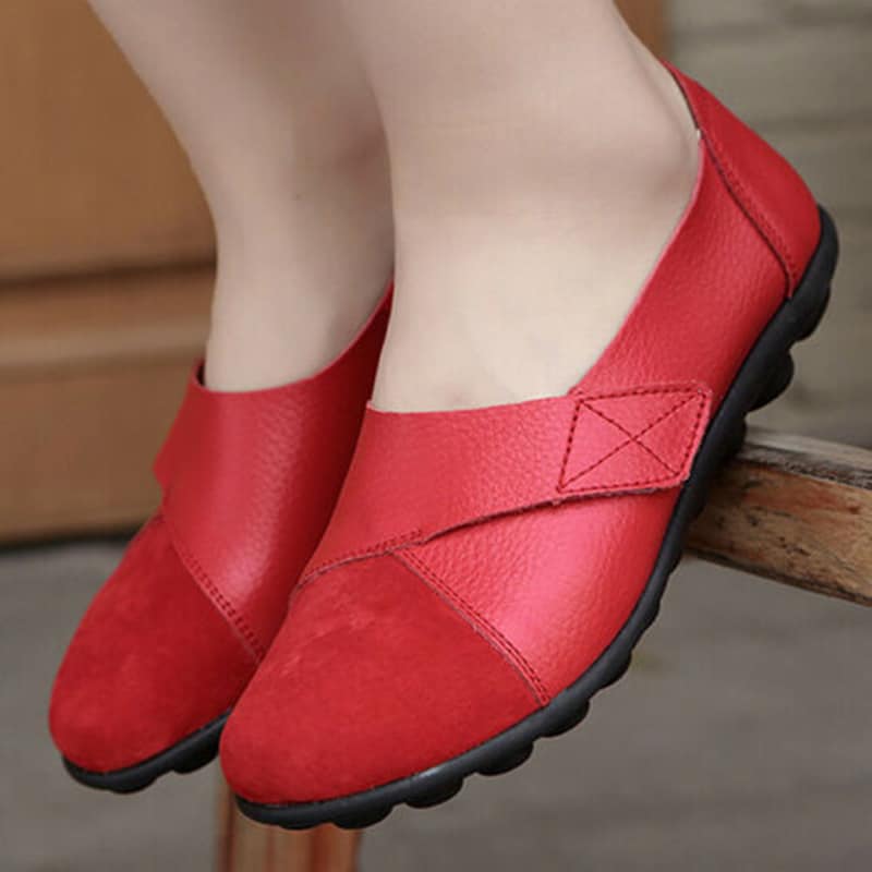 On voit une paire de pieds blancs chaussés de mocassins rouges avec une bride à scratch.