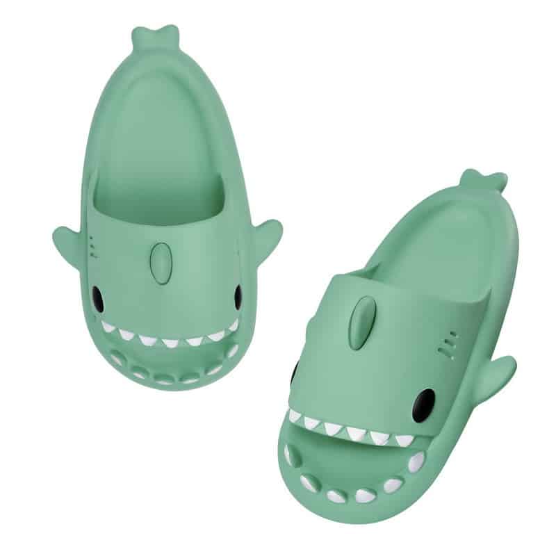 Des tongs orthopédiques verte avec une tête de requin à dents blanches sur un fond blanc.